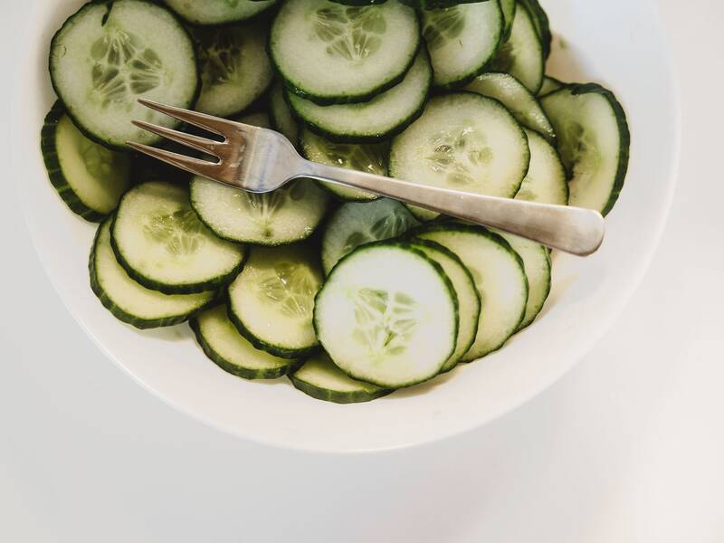 Blick auf eine Schüssel mit einer in Scheiben geschnittenen Salatgurke, oben drauf liegt eine Gabel