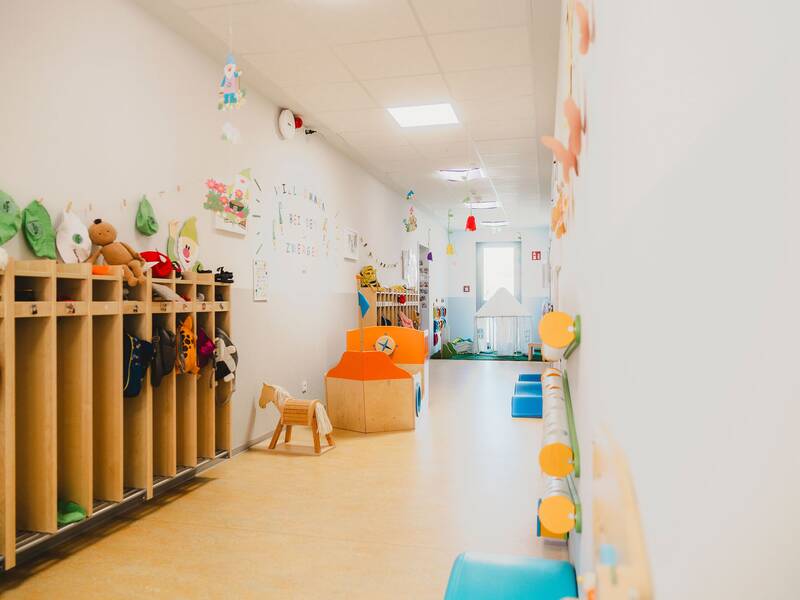 Blick auf den Flur, an der einen Wand stehen die Garderoben für die Kinder, an der gegenüberliegenden Wand sind Spielmöglichkeiten für die Kinder befestigt