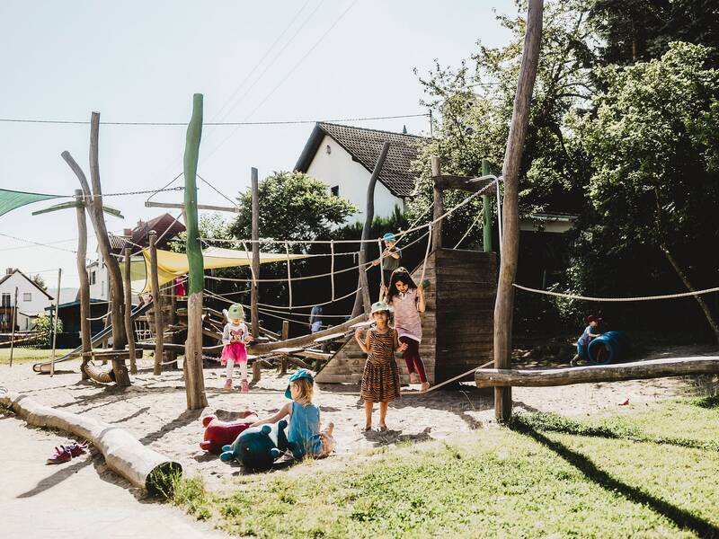Blick auf den Spielplatz wo mehrere Kinder vor einem Kletterspielgerät im Sand spielen
