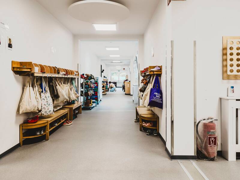 Blick in den Flur, an den Wänden sind die Garderoben für die Kinder befestigt. An der Garderoben hängen die Taschen der Kinder und die Schuhe sind unten im Schuhfach