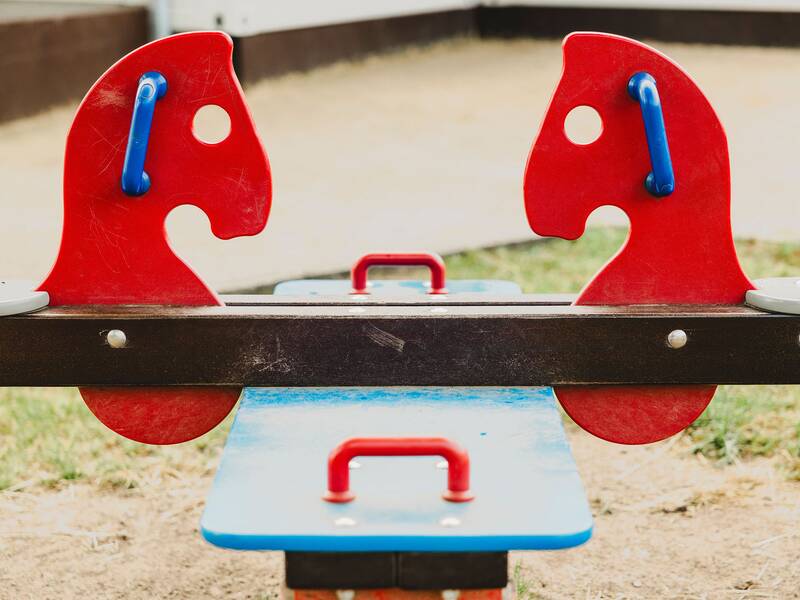 Blick auf eine Kinderwippe mit zwei roten Pferdeköpfen und blauen Haltegriffen