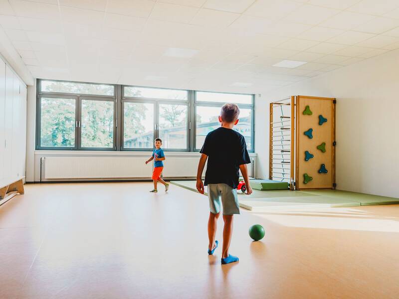 zwei Jungs spielen im Turnraum zusammen mit einem grünen Ball
