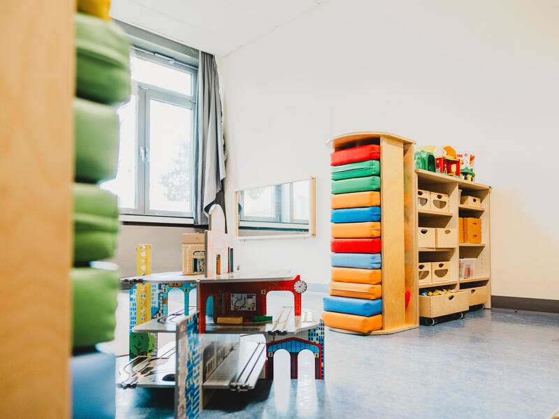 Blick in den Gruppenraum und auf einen Spielschrank in dem seitlich bunte Kunststoffkissen übereinander gestapelt sind