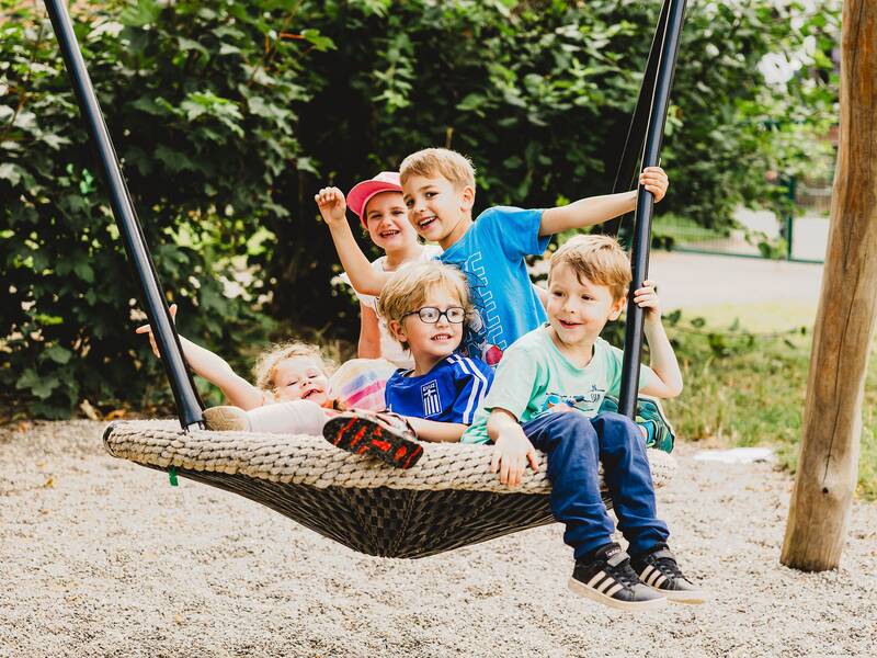 fünf fröhliche Kinder sitzen zusammen in einer Nestschaukel und schaukeln