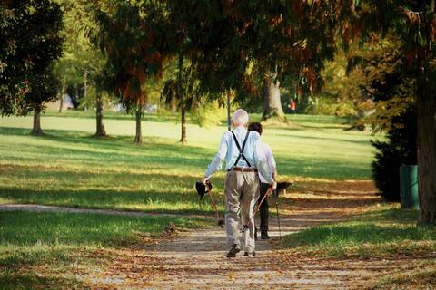 Ein älteres Paar, Mann und Frau, machen gemeinsam Nordic Walking. Die Frau geht voran und der Mann folgt ihr. Die Frau ist größtenteils verdeckt.